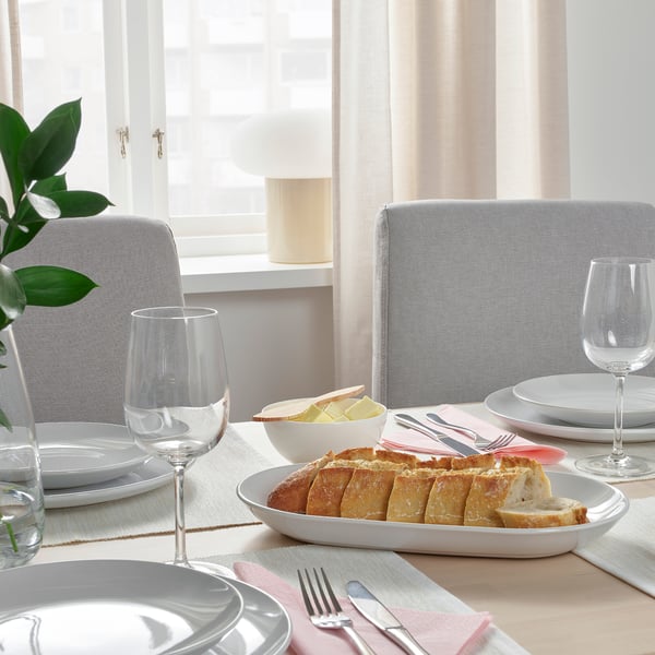 Mise en place de la table avec des assiettes, des verres, du pain et du beurre sur une nappe blanche.