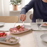 Personne servant du prosciutto et des tomates dans un plat blanc sur une table élégante.