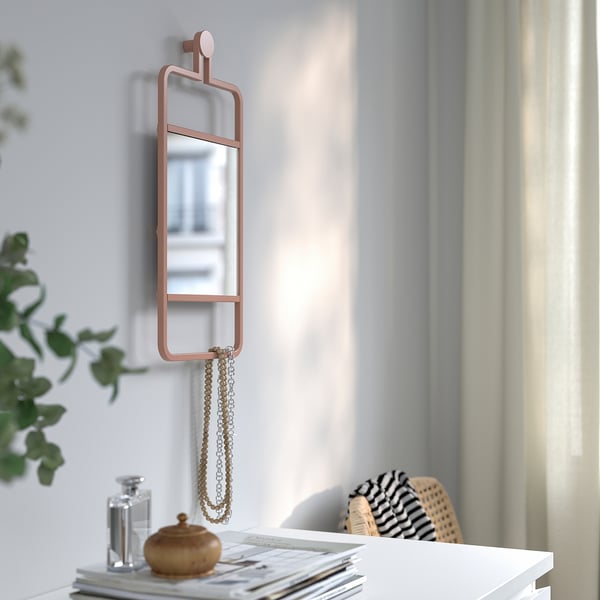 Un miroir mural avec un cadre en cuivre et une étagère en dessous, contenant un collier et une bouteille.