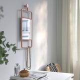 Un miroir mural avec un cadre en cuivre et une étagère en dessous, contenant un collier et une bouteille.