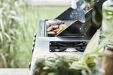 Gril argenté en cours d’utilisation, cuisson des aliments à l’extérieur avec de la verdure en arrière-plan.
