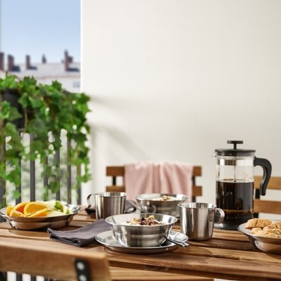 Table d’extérieur avec ustensiles GRILLTIDER en acier inoxydable, y compris des bols, des tasses et une presse à café.
