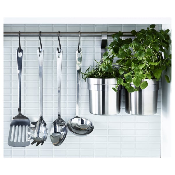 Une tringle de cuisine avec des cuillères métalliques, une louche, une spatule et des herbes dans des pots.