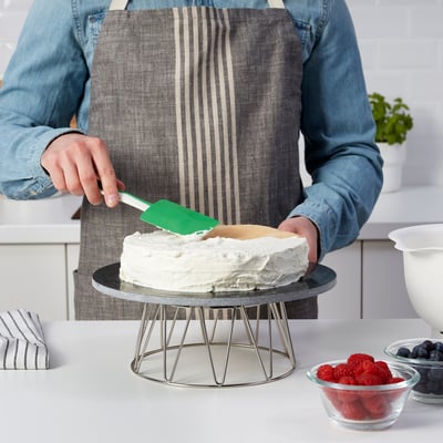 Glaçage personne gâteau avec spatule verte. Gâteau sur support en métal, baies à proximité.
