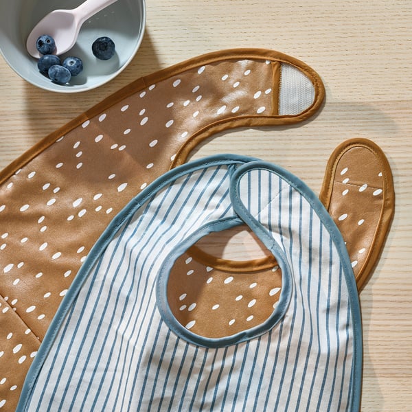 Deux bavoirs pour bébé à motifs sur une surface en bois. L’un avec des rayures, l’autre avec des pois. Les façades sont imperméables, les dos sont en coton doux.