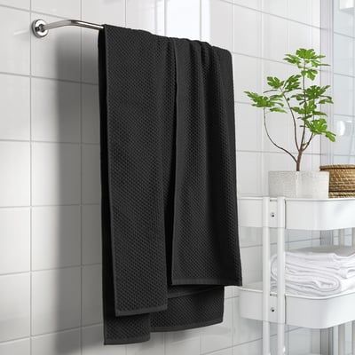 Trois serviettes noires GULVIAL sont accrochées au mur d’une salle de bain, avec une fougère en pot ajoutant de la verdure à l’espace propre et organisé.