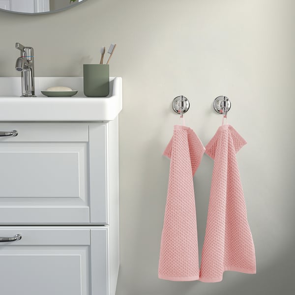 Lavabo blanc, robinet argenté, tasse verte avec brosses à dents, deux serviettes GULVIAL beiges sur crochets chromés.