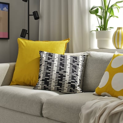 Scène de salon avec canapé gris, affichant de grands coussins jaunes, à motifs et à pois. Plante et décoration à proximité.