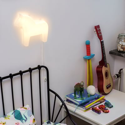 Lampe de chevet en forme de tête de cheval éclairant une chambre d’enfant avec des jouets et des livres sur une table de chevet.