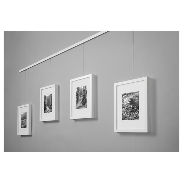 Quatre photos de nature en noir et blanc sont accrochées dans des cadres blancs sur un mur gris à l’aide d’un système de rail de suspension blanc réglable.