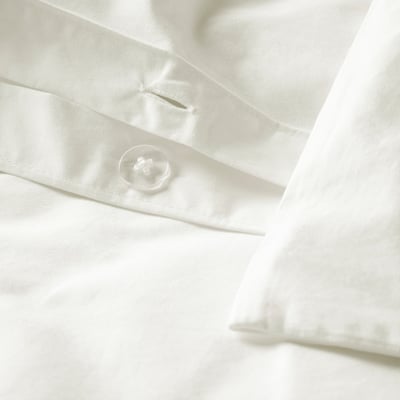 Gros plan sur du linge de lit blanc impeccable avec un seul bouton blanc proéminent. Le tissu présente des coutures fines et une texture luxueuse et lisse.