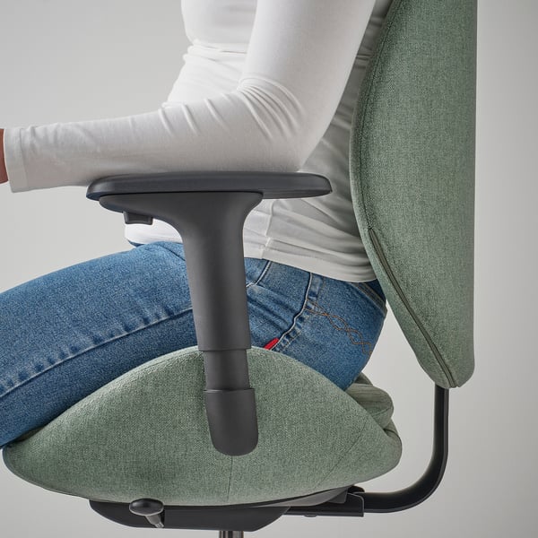 Personne assise sur une chaise de bureau ergonomique verte, montrant des accoudoirs réglables et un siège rembourré.