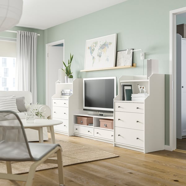 Mobilier HAUGA blanc de salon moderne, y compris un meuble TV et des commodes avec tiroirs, complétant les murs vert clair et les planchers en bois.