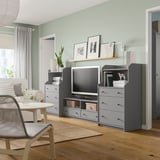 Salon moderne avec des murs verts, des planchers en bois clair, des unités de rangement HAUGA grises, une télévision, des plantes et un décor minimaliste.