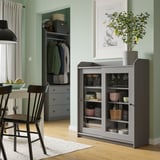 Salle à manger moderne avec armoire HAUGA grise exposant de la vaisselle, des chaises noires et des murs verts.