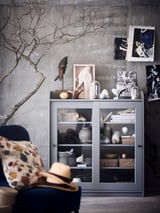 Salon moderne avec armoire HAUGA grise exposant des œuvres d’art, des objets décoratifs et des plantes.
