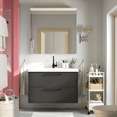 Salle de bain moderne avec meuble-lavabo flottant noir HAVBÄCK, comptoir blanc, grand miroir et chariot de rangement blanc.