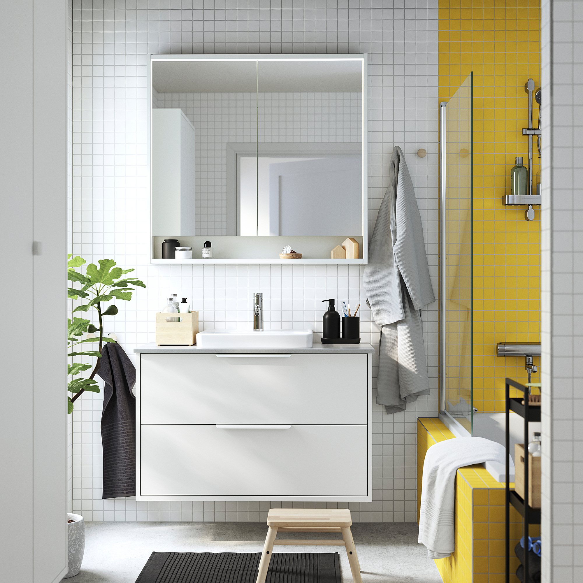Salle de bains moderne avec meuble-lavabo HAVBÄCK, lavabo semi-encastré, miroir, serviettes, plante et douche en carrelage jaune.