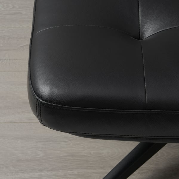 Gros plan d’un repose-pieds moderne en cuir noir sur un plancher en bois, mettant en valeur son design lisse et élégant.
