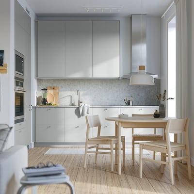 Cuisine moderne avec armoires HAVSTORP grises, surfaces élégantes, parquet et ensemble de salle à manger compact sous la fenêtre.