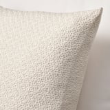 Coussin beige avec texture tricotée, toucher coton doux, fermeture à glissière visible.