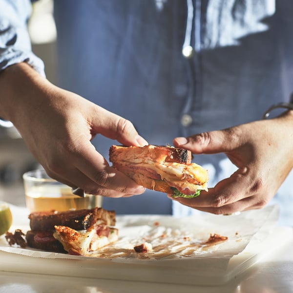 Les mains tenant un sandwich au petit-déjeuner, mettant en valeur une répartition uniforme de la chaleur et une manipulation facile sur toutes les plaques de cuisson.