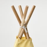 Poteaux de tente en bois attachés ensemble, insérés dans un sac en tissu jaune.