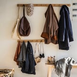 Un porte-manteau en bois, HÖVOLM, avec des vestes, des sacs et des accessoires. Il a une finition en chêne naturel et est monté sur un mur.
