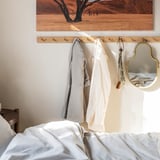 Chambre avec lit blanc, porte-manteau en chêne, serviettes grises et blanches, miroir doré, art du désert.