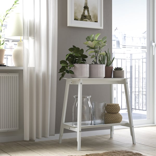 Chambre grise avec support de plantes contenant des pots. Vases transparents, paniers, rideaux, radiateur et balcon.