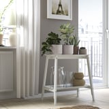 Chambre grise avec support de plantes contenant des pots. Vases transparents, paniers, rideaux, radiateur et balcon.