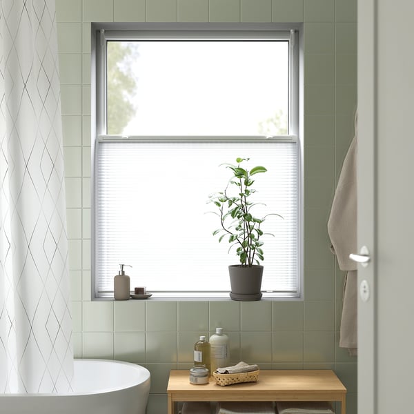 Salle de bain moderne avec grande fenêtre, store HORNVALLMO, plante, serviettes, carreaux verts.