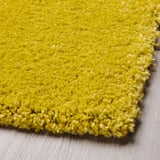 Tapis texturé jaune vif en gros plan sur le parquet. Doux et à poils longs visibles, offrant confort et chaleur.