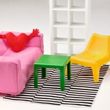 Configuration miniature de la chambre d’enfant avec canapé rose vif, coussin coeur rouge, table verte, chaise jaune et tapis rayé noir-blanc.