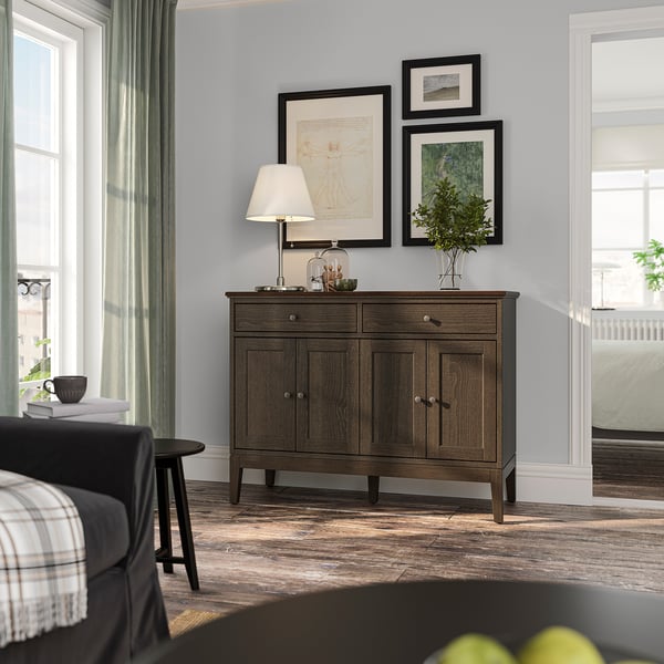 Chambre moderne : buffet IDANÄS avec portes pliantes et cadres d’art décoratifs. Éclairage tamisé, bois sombre, décor calme.