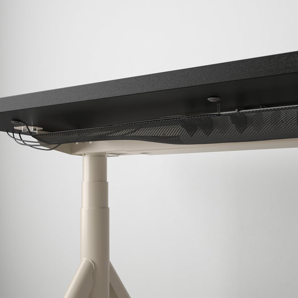Bureau noir avec fonction de réglage de la hauteur, poignée de commande visible et filet de gestion des câbles en dessous.