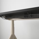 Bureau noir avec fonction de réglage de la hauteur, poignée de commande visible et filet de gestion des câbles en dessous.