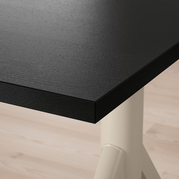 Gros plan d’un coin de bureau élégant, noir et moderne ; La surface lisse et sombre reflète la lumière, soutenue par des pieds en métal robustes.