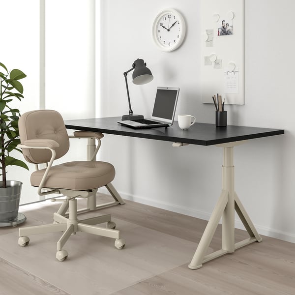 Bureau ajustable IDÅSEN noir, base blanche, chaise beige, lampe, ordinateur portable, tasse et tableau blanc. Espace de travail soigné et efficace pour le travail et les études.
