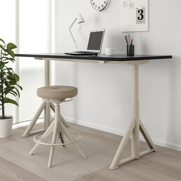 Bureau IDÅSEN blanc/noir avec ordinateur portable, lampe, tabouret sur parquet. Réglable en hauteur.