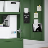 Armoire IDÅSEN verte avec porte ouverte, montrant des boîtes de rangement, des papiers et des notes sur la porte.