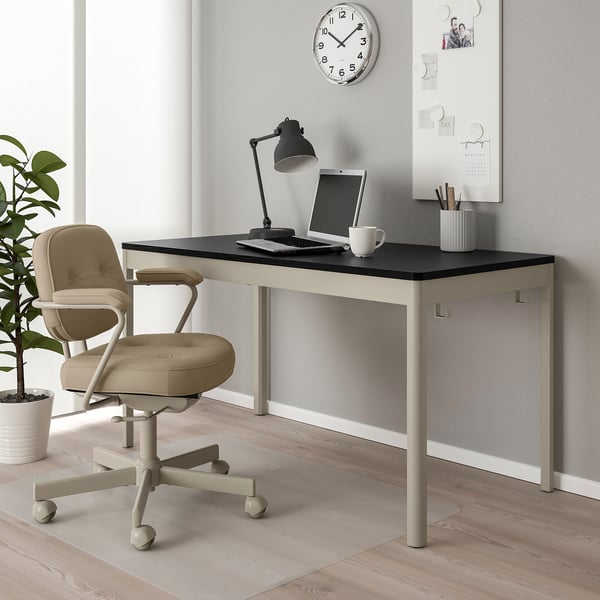 Bureau IDÅSEN avec ordinateur, lampe et chaise. Le mur a un tableau blanc et une horloge. La plante ajoute de la verdure.