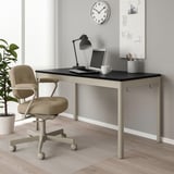 Bureau IDÅSEN avec ordinateur, lampe et chaise. Le mur a un tableau blanc et une horloge. La plante ajoute de la verdure.