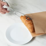 Pince ramassant une pâtisserie dans un sac en papier brun au-dessus d’un bol blanc.