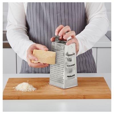 La personne râpe le fromage à l’aide d’une râpe en acier inoxydable à deux côtés sur une planche à découper en bois.