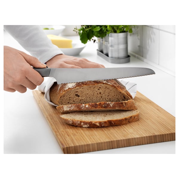 Personne coupant du pain avec un couteau dentelé sur une planche à découper en bois.