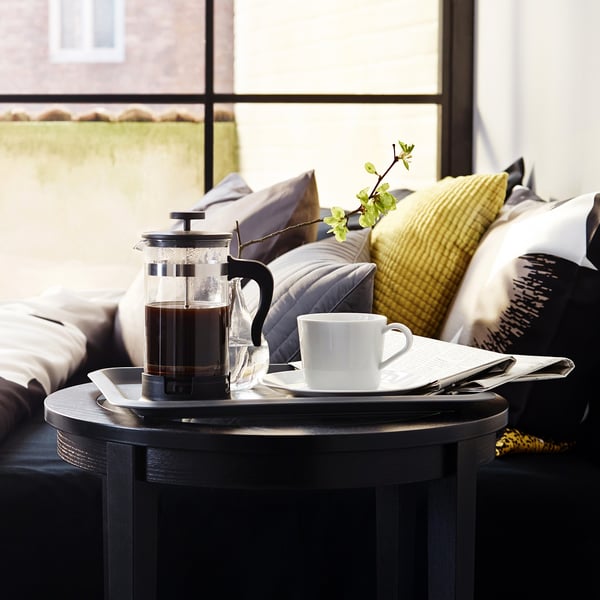 Presse à café moderne sur table noire avec tasse, offrant du café frais, posé près douillet banc rembourré.