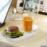 Un repas avec un sandwich rempli de verdure et un verre de jus d’orange sur une assiette blanche.
