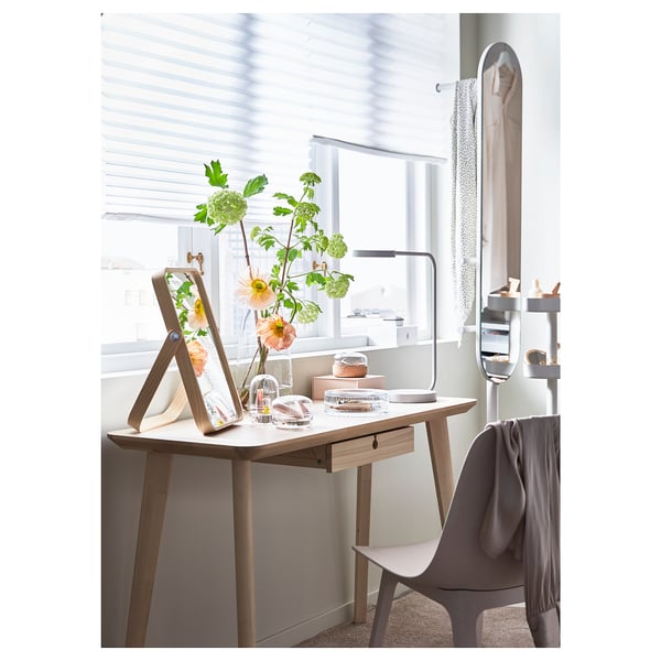 Bureau moderne avec bois clair et chaise grise ; fleurs, lampe et miroir ; Chambre lumineuse et bien rangée.