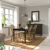 Salle à manger confortable avec une table extensible noire INGATORP, des chaises en bois et un tapis. Près de la fenêtre avec rideaux, armoire sombre avec miroir.